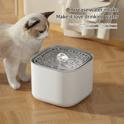 A cat looking at a white AquaPurr Refreshing Cat Water Fountain with water in it, placed on a wooden floor.