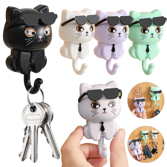 A collection of cat-shaped keys hooks in black, white, and green colors, each wearing sunglasses and holding a key. The hooks are designed to be cute and functional for organizing items such as keys, towels, and coats.