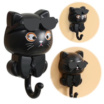 A set of images showing a black cartoon cat-shaped keys hook with sunglasses, first from the front and then from the side, against a yellow background.
