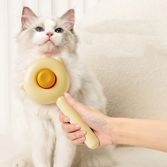 A person holding a yellow cat grooming brush, with a white cat looking at it curiously.