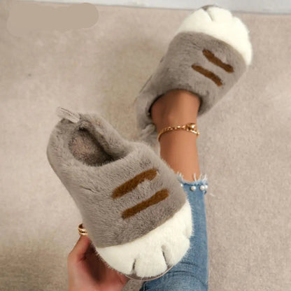 A pair of gray cat paw-shaped plush home slippers with a 3D design, worn by a person with the ankle area visible.