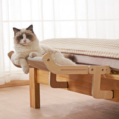 A cat resting on a hanging window bed attached to a wooden frame, with a clear view of the outside environment.