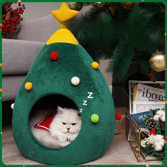 A white cat resting inside a green Christmas tree-shaped plush pet bed with festive ornaments.
