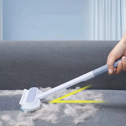 A hand using a white brush with a gray handle on a couch, with highlighted areas showing the cat hair being removed.