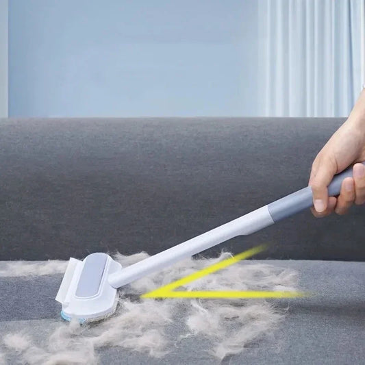 A hand using a white brush with a gray handle on a couch, with highlighted areas showing the cat hair being removed.