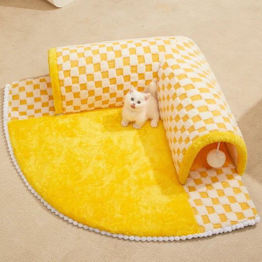 A small white cat sitting inside a yellow and white checkered cat hideaway with a ball toy in the corner.