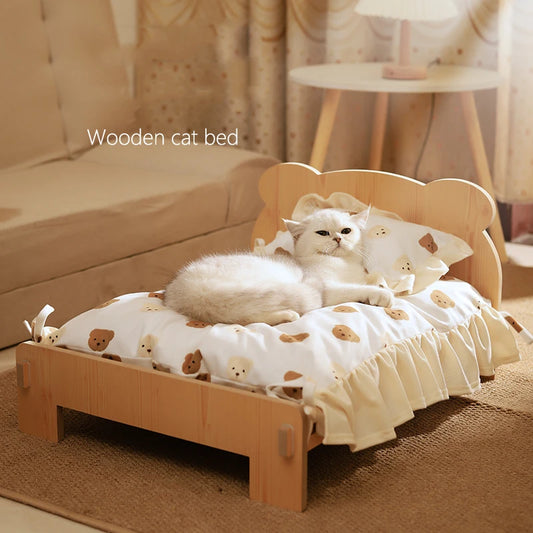 A white cat with a teddy bear design on the bedding, resting on a wooden cat bed with a brown and white blanket.