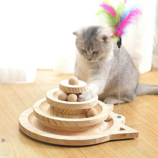 A cat playing with a triple-level wooden cat toy tower, with balls rolling down the tracks on a table.