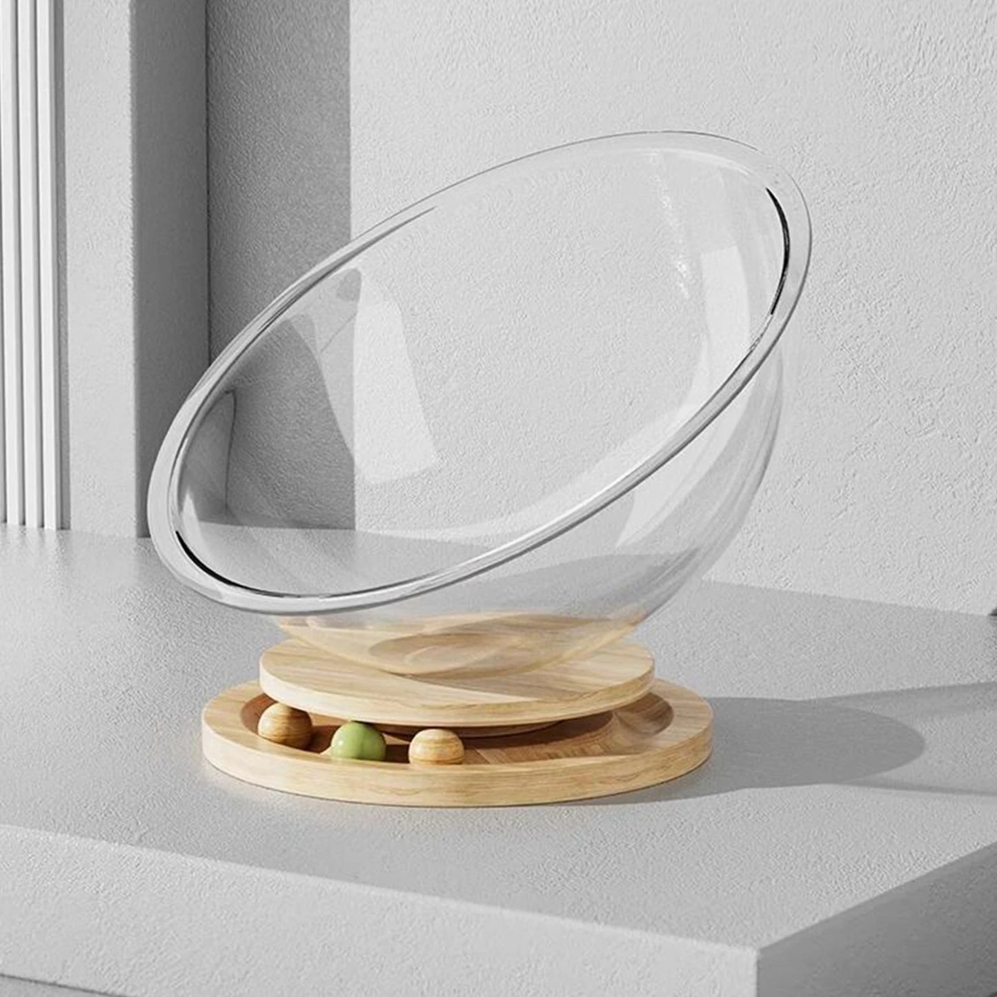 A clear, round capsule-shaped cat bed with a wooden base, placed on a marble surface with a blurred background.