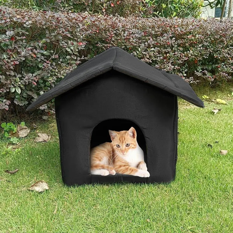 A waterproof outdoor pet house with a black roof, featuring a cozy interior where a cat is resting. The pet house is placed on grass with shrubbery in the background.